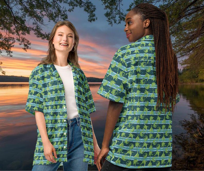 May include: Two people wearing short-sleeved button-down shirts with a repeating pattern of green dinosaurs on a dark blue background with horizontal light blue stripes. The shirts are open, revealing a white t-shirt underneath. The background shows a sunset over a lake.