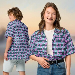 May include: Short-sleeved button-down shirt with a repeating pattern of pink and teal sea creatures on a dark teal and white striped background. The shirt is worn by two people, one facing the camera and the other with their back to the camera.