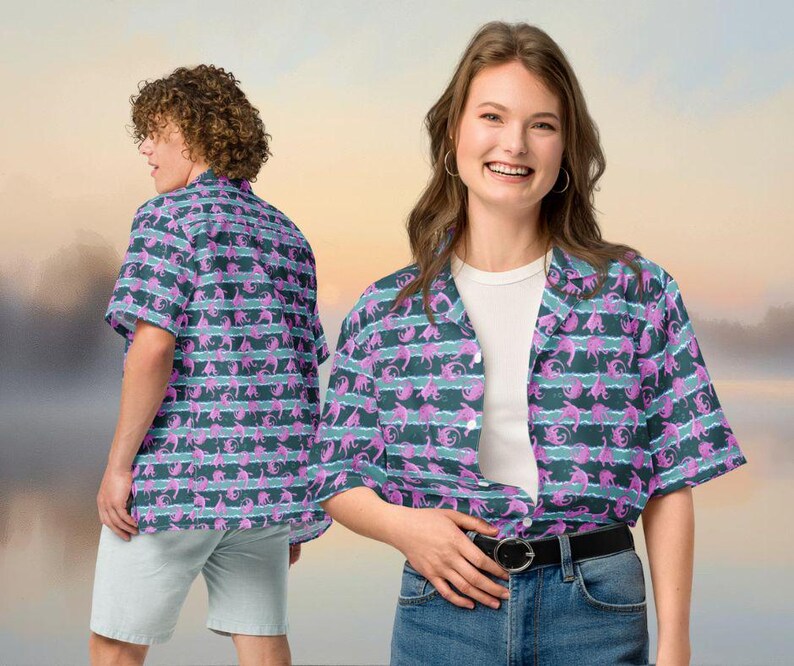 May include: Short-sleeved button-down shirt with a repeating pattern of pink and teal sea creatures on a dark teal and white striped background. The shirt is worn by two people, one facing the camera and the other with their back to the camera.