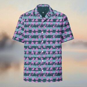 May include: Short-sleeved button-down shirt with a repeating pattern of pink creatures on a dark teal background. The design includes horizontal stripes of light teal. The shirt has a classic collar and white buttons.
