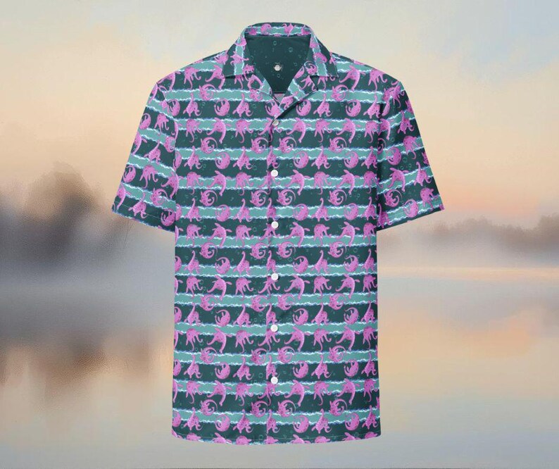 May include: Short-sleeved button-down shirt with a repeating pattern of pink creatures on a dark teal background. The design includes horizontal stripes of light teal. The shirt has a classic collar and white buttons.