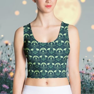 May include: A dark teal crop top with a repeating pattern of green crescent moons, stars, and stylized floral elements. The top has a scoop neckline and is made of a soft, stretchy fabric. The overall theme is celestial and botanical.