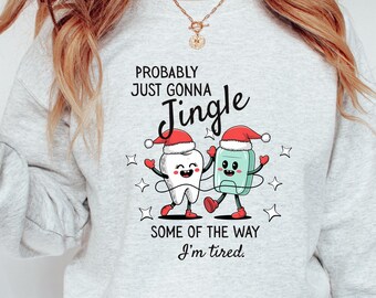 May include: Light gray sweatshirt with a festive graphic featuring a cartoon tooth and a mouthwash bottle wearing Santa hats. Text reads "Probably Just Gonna Jingle" and "Some of the way I'm tired."