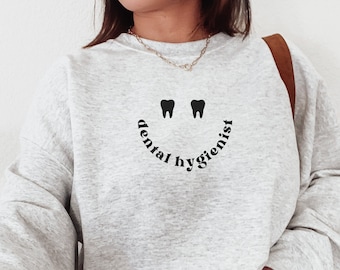 May include: A gray sweatshirt with a black graphic of a smiley face made of teeth and the text "dental hygienist".