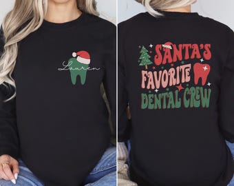 May include: Black long-sleeve shirt with a Christmas-themed design. The front features a green tooth with a Santa hat and the name "Lauren". The back features a green Christmas tree, a red tooth, and the text "Santa's Favorite Dental Crew".