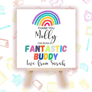 May include: A white card on a wooden easel with a rainbow and the words "Thank You Molly for being a Fantastic Buddy Love from Sarah." The background has colorful school-themed doodles.