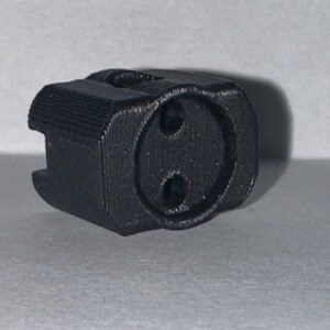 May include: A black plastic electrical outlet adapter with two round holes.