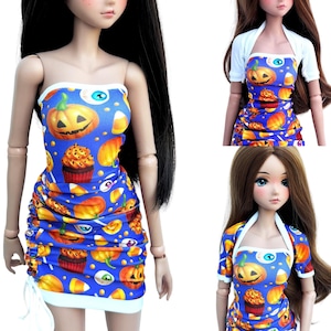 May include: A doll wearing a strapless blue dress with a Halloween print featuring jack-o'-lanterns, cupcakes, candy corn, and eyeballs. The dress has white trim and a ruched side with a white drawstring. Some views show a white short-sleeve bolero.