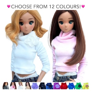 Puede incluir: Dos muñecas con jerséis de cuello alto de diferentes colores. La muñeca de la izquierda lleva un jersey blanco y la muñeca de la derecha lleva un jersey rosa. Las muñecas llevan vaqueros y tienen el pelo largo. La imagen muestra una variedad de colores para los jerséis, incluyendo gris, rosa, blanco, morado, negro, azul, rojo, verde y amarillo.