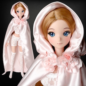 Könnte beinhalten: Puppe mit blonden Haaren und blauen Augen, bekleidet mit einem hellrosa Satin-Kapuzenmantel mit floralen Akzenten. Die Puppe trägt auch ein weißes Spitzen-Outfit, einschließlich Shorts, Oberteil und Oberschenkel-Socken. Es ist ein Sammlerstück.