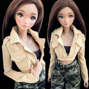 May include: A beige cropped jacket with a zip fastening and two large pockets. The jacket is worn over a black vest top and camouflage trousers.
