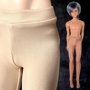 Op de afbeelding: Close-up van een beige panty met een textuurpatroon. Een pop met een neutrale huidskleur, grijs haar en rode ogen staat naast de panty. De pop draagt een bijpassende beige panty.