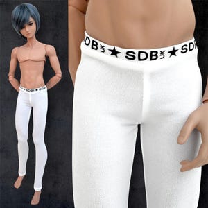 Op de afbeelding: Witte legging met een zwarte tailleband met de tekst "SDB" en sterren. De legging is nauwsluitend en lijkt gemaakt van een zachte, getextureerde stof. De tailleband is zichtbaar bij de taille.