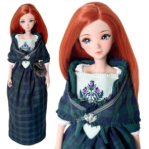Könnte beinhalten: Puppe mit langen roten Haaren und blauen Augen, gekleidet in einem grün-blauen karierten Kleid und Schal. Das Kleid hat ein weißes Oberteil mit lila Blumenstickerei und eine kleine braune Tasche.
