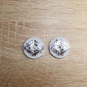 May include: A pair of silver earrings with a geometric design. The earrings are round and have a sparkly finish.