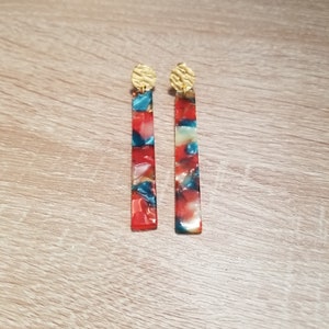 Peut inclure: Une paire de longues boucles d'oreilles à motifs rouges, bleus et blancs avec des sommets dorés.