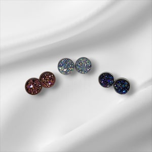 Peut inclure: Trois paires de petites boucles d'oreilles rondes et scintillantes. Les boucles d'oreilles sont dans des tons de rose, bleu et violet.