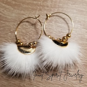May include: A pair of gold hoop earrings with white fluffy fur pom-poms attached. The fur is arranged in a fan shape and the hoops have small gold beads.
