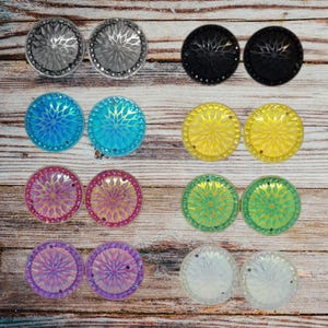 May include: Assortment of 10 pairs of round, decorative, iridescent, and clear cabochons. The cabochons have a starburst design and come in a variety of colors, including silver, black, blue, yellow, pink, green, and purple.