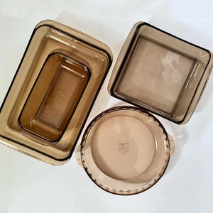 May include: Set of four brown glass baking dishes. The dishes are nested inside each other. The largest dish is a rectangular loaf pan, the next is a smaller rectangular dish, the next is a square dish, and the smallest is a round pie dish.
