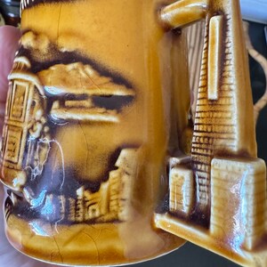 May include: A brown ceramic mug with a raised design of a cable car and the Golden Gate Bridge. The mug has the word "SAN FRANCISCO" written on the front.