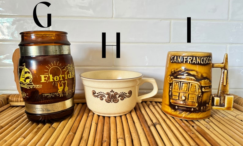 May include: Three ceramic mugs with different designs. The first mug is brown with a gold band and says "Florida" on it. The second mug is cream colored with a brown floral design. The third mug is brown with a picture of a San Francisco cable car and says "San Francisco" on it.