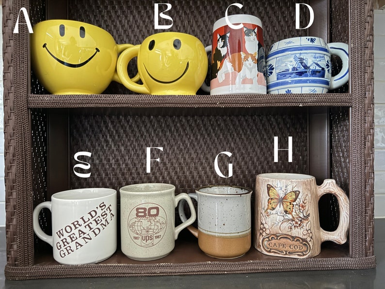 May include: A shelf with eight ceramic mugs. The mugs are decorated with various designs, including smiley faces, cats, a windmill, a globe, a butterfly, and the words "World's Greatest Grandma".