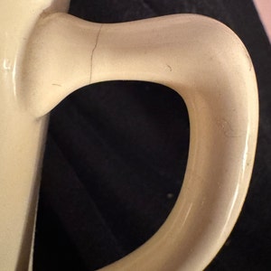 May include: Close-up of a cream-colored ceramic mug handle with a slight crack. The handle is smooth and rounded.