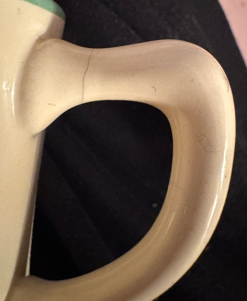 May include: Close-up of a cream-colored ceramic mug handle with a slight crack. The handle is smooth and rounded.