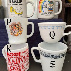 May include: Five white ceramic mugs with different designs. The mugs are arranged in a circle. The mugs have the following designs: "TGIF Thank Goodness It's Full", a rainbow with the text "Would You Believe I Graduated?", a tiger, a blue and white floral pattern, and a red and white pattern with the text "Kaffee, Cafe, Kopi, Kahvi".
