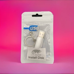 May include: A silver USB flash drive with a clear cap and keyring attachment, packaged in a clear plastic bag. The bag has a blue USB label and a small sticker with the text "openSUSE Install Disk" and a chameleon logo.