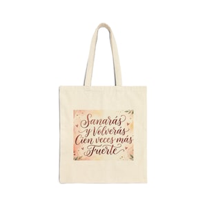 Puede incluir: Un bolso tote de color crema con un diseño rectangular que presenta el texto "Sanarás y Volverás Cien veces más Fuerte" en una elegante escritura. El diseño tiene un efecto acuarela con tonos rosas y melocotón, y pequeños acentos de corazón y hoja.
