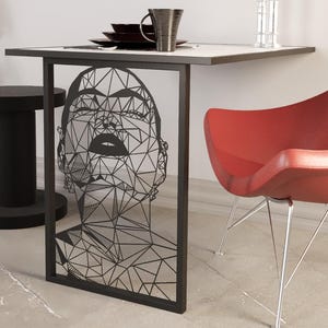 May include: A contemporary dining set with a black metal table featuring a geometric face design. The set includes a red chair with silver legs, a black side table, and a potted plant. Table dimensions are approximately 76 cm long.