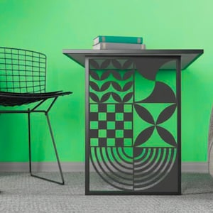 Pode incluir: Uma mesa lateral de metal preto com um tampo retangular e um painel lateral decorativo com um padrão geométrico de círculos, quadrados e linhas. Dois livros azul-petróleo estão empilhados na superfície plana da mesa.