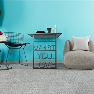 May include: A modern side table with a black metal frame and a gray top. The frame features the words "DO WHAT YOU LOVE" cut out. A black chair, a gray armchair with a white pillow, and decorative items are also visible.