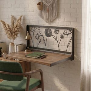 Peut inclure: Un bureau mural composé d'un plateau rectangulaire en bois et d'un cadre arrière en métal noir avec un motif floral découpé au laser. Le bureau est fixé à un mur en briques blanches, offrant une surface de travail plane pour écrire.