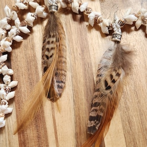 May include: A pair of feather earrings with silver accents. The feathers are brown and white with a hint of orange. The earrings are hanging from a strand of white and brown seashells.