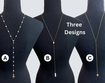 May include: Three gold-toned lariat necklaces displayed on black mannequins. Necklace A features heart-shaped charms and a gold arrow pendant. Necklace B has a single pearl and three pearls. Necklace C has a gold arrow pendant.