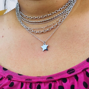 May include: A silver star pendant necklace with multiple silver chain layers. The necklace is layered on a person's neck.