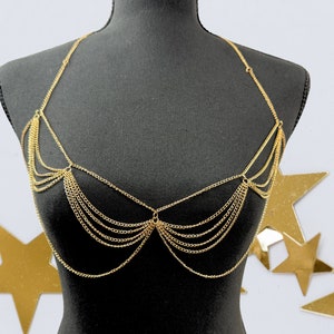 May include: Gold chain body jewelry with multiple layers of chains forming a delicate and intricate design. The jewelry is displayed on a black mannequin.
