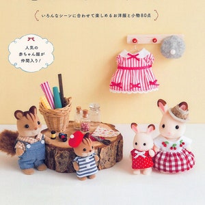 Puede incluir: Un libro con una portada rosa y amarilla que presenta una muñeca Sylvanian Families con un vestido rojo y blanco. El título del libro es "Sylvanian Families: Coser ropa para tu familia". La portada del libro también incluye una pequeña ilustración de una muñeca ardilla con una camisa a rayas azul y blanca y una boina roja.