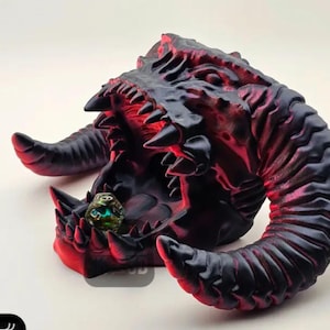 May include: A red and black dragon head dice tower with a green and silver dice inside the mouth. The dragon has sharp teeth and horns.