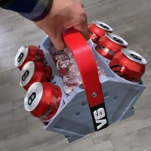 May include: A gray six-pack cooler with a red handle. The cooler is filled with ice and six cans of soda. The cooler has the text "V6" printed on the side.