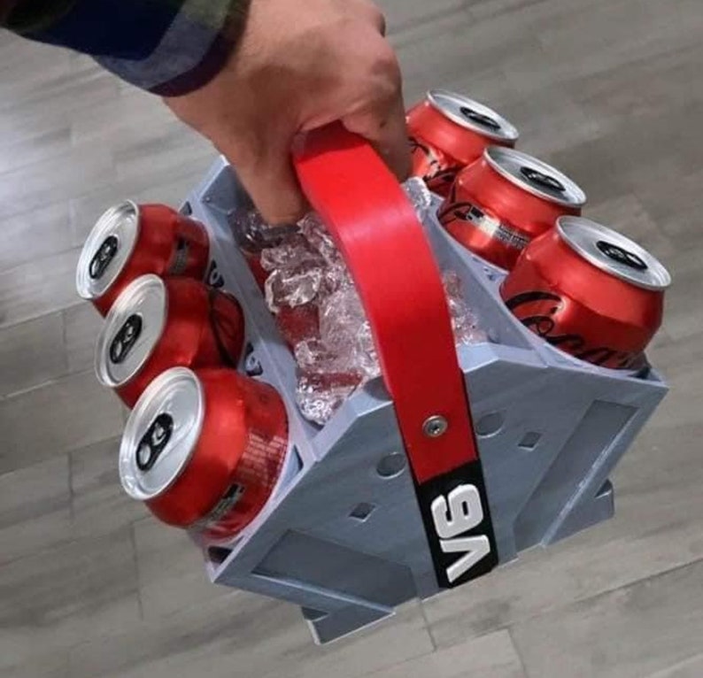 May include: A gray six-pack cooler with a red handle. The cooler is filled with ice and six cans of soda. The cooler has the text "V6" printed on the side.