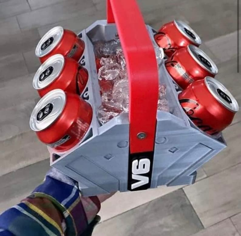 May include: A gray six-pack cooler with a red handle. The cooler is filled with ice and six red cans of soda. The cooler has the word "V6" printed on the side.