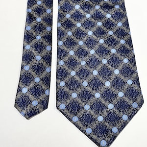 May include: A navy blue necktie with a repeating pattern of light blue polka dots within a grid of tan and navy blue. The tie is made of a textured fabric and is displayed on a white background.