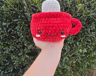 May include: A red crocheted mug with a white crocheted marshmallow on top. The mug has a happy face with black eyes and a smile.
