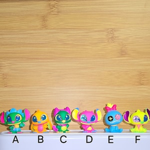 May include: Six colorful Stitch figurines, each with a different expression and color scheme. The figurines are arranged in a row on a wooden surface, labeled A through F.