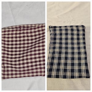 Puede incluir: Dos artículos de tela con estampados de cuadros. Uno es un patrón de cuadros burdeos y crema, y el otro es un patrón de cuadros azul marino y crema. Ambos son rectangulares y parecen estar hechos de algodón o un material similar.