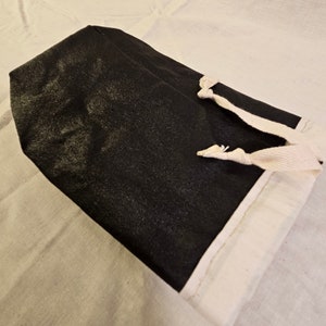 Può includere: Una borsa in tessuto nero con finiture bianche e chiusura con coulisse. La borsa è rettangolare con una superficie strutturata. Il cordino è realizzato in materiale bianco tessuto.